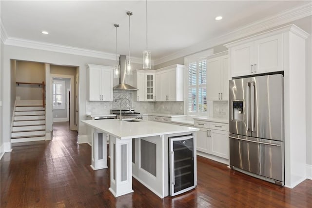 kitchen with decorative light fixtures, an island with sink, stainless steel fridge, beverage cooler, and wall chimney exhaust hood