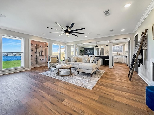 living room featuring sink, ceiling fan, hardwood / wood-style floors, decorative columns, and ornamental molding