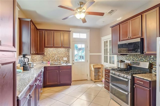 kitchen with stainless steel appliances, light tile patterned flooring, light stone countertops, and sink