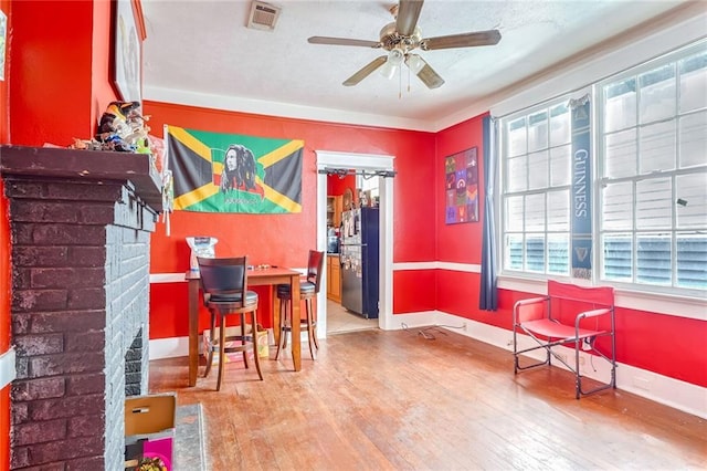 interior space with ceiling fan, plenty of natural light, a brick fireplace, and light hardwood / wood-style flooring