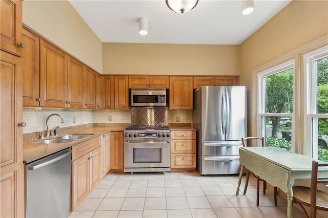 kitchen with appliances with stainless steel finishes, sink, decorative backsplash, light tile patterned floors, and light stone countertops