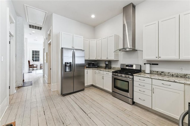 kitchen with wall chimney range hood, white cabinetry, stainless steel appliances, light hardwood / wood-style floors, and light stone countertops