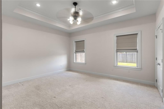 spare room featuring a tray ceiling, light colored carpet, and ceiling fan