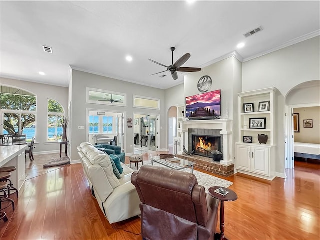 living room with crown molding, ceiling fan, a fireplace, and hardwood / wood-style flooring