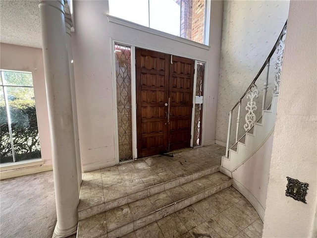 entrance foyer featuring decorative columns, a towering ceiling, and a textured ceiling