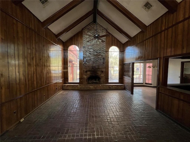 unfurnished living room with beamed ceiling, a brick fireplace, high vaulted ceiling, and wood walls