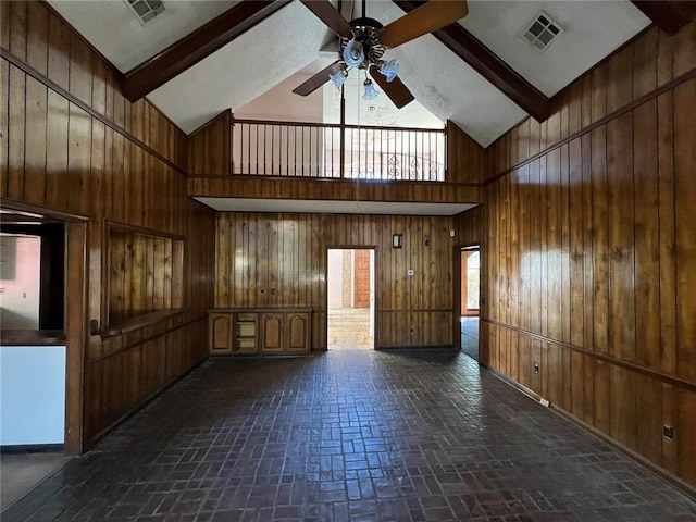 empty room featuring beamed ceiling, high vaulted ceiling, and wood walls