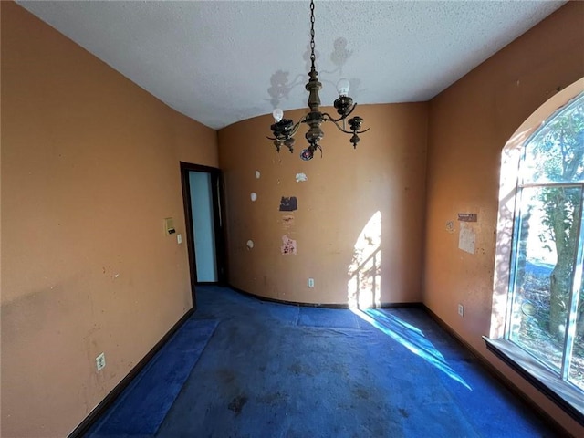 unfurnished room featuring dark colored carpet, an inviting chandelier, and a textured ceiling