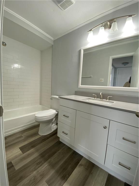 full bathroom with tiled shower / bath, wood-type flooring, vanity, ornamental molding, and toilet