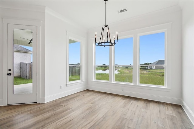 unfurnished dining area featuring a water view, an inviting chandelier, and light hardwood / wood-style flooring