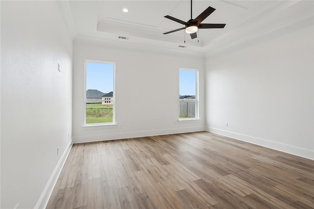 spare room featuring a raised ceiling, ceiling fan, ornamental molding, and light wood-type flooring