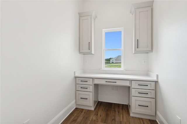 unfurnished office featuring dark hardwood / wood-style flooring and built in desk