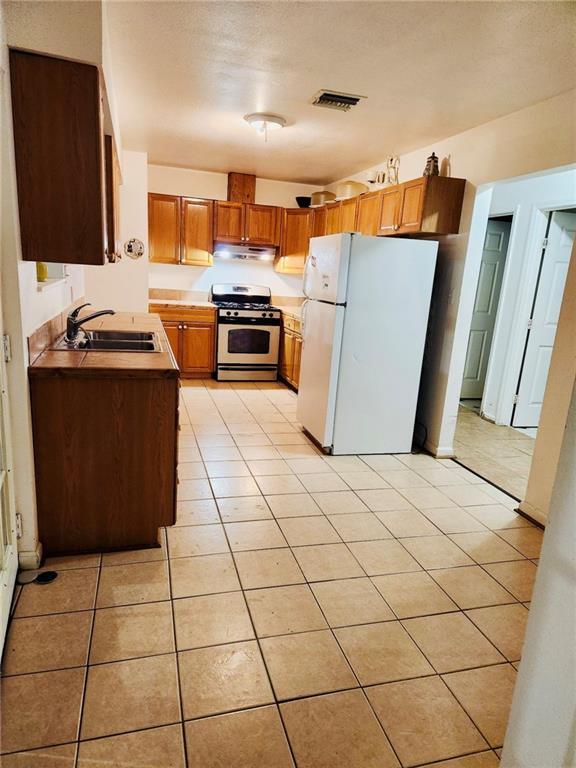 kitchen with sink, white fridge, light tile patterned floors, stainless steel gas range, and a textured ceiling