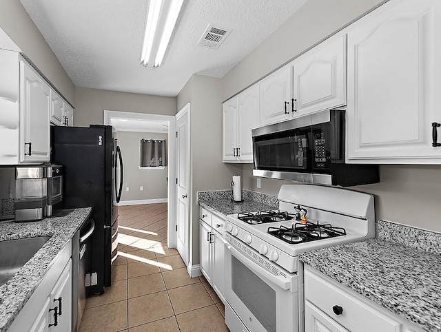 kitchen featuring appliances with stainless steel finishes, light tile patterned floors, white cabinets, and light stone counters