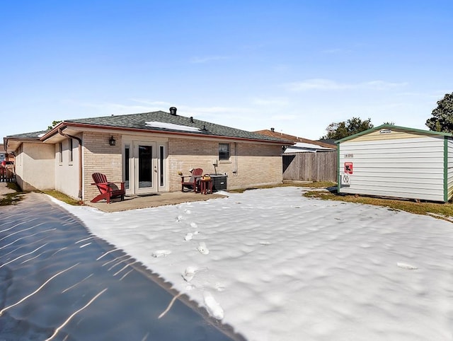 snow covered rear of property with a shed and a patio