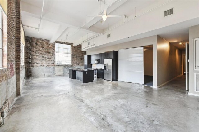 basement with visible vents, a ceiling fan, stainless steel fridge, and brick wall