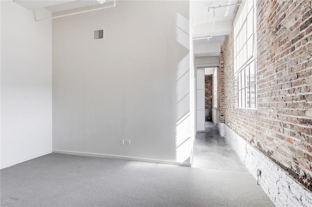 interior space with baseboards, visible vents, a towering ceiling, and brick wall