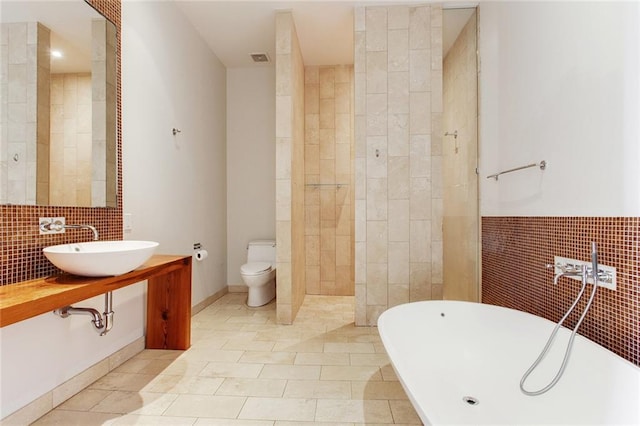 bathroom featuring tile walls, a soaking tub, toilet, a sink, and a walk in shower