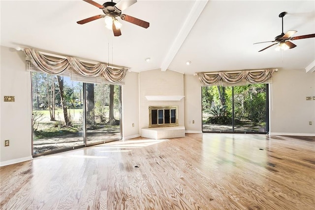 unfurnished living room featuring a tiled fireplace, hardwood / wood-style floors, plenty of natural light, and lofted ceiling with beams