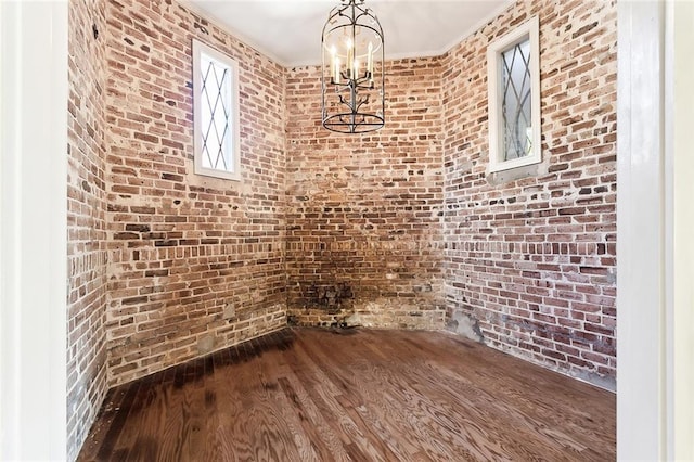 unfurnished dining area featuring dark wood-type flooring, ornamental molding, and brick wall