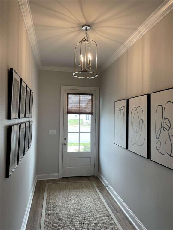 doorway to outside featuring wood-type flooring, ornamental molding, and a chandelier