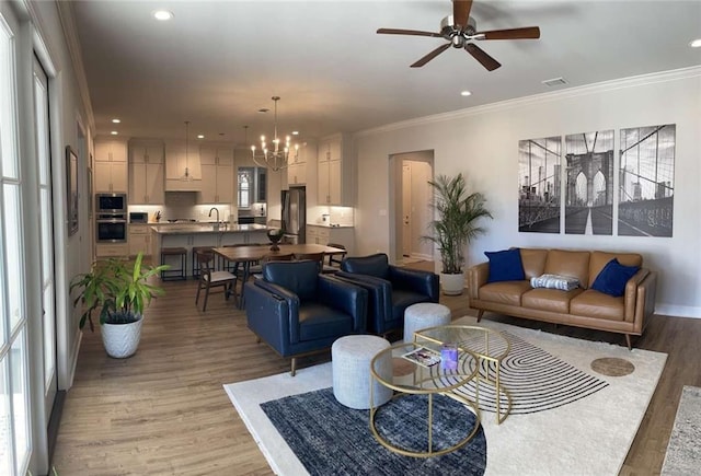 living room featuring sink, ceiling fan with notable chandelier, light hardwood / wood-style flooring, and ornamental molding