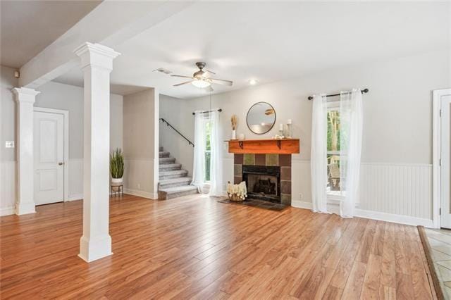 unfurnished living room with light hardwood / wood-style flooring, a tile fireplace, ceiling fan, and ornate columns