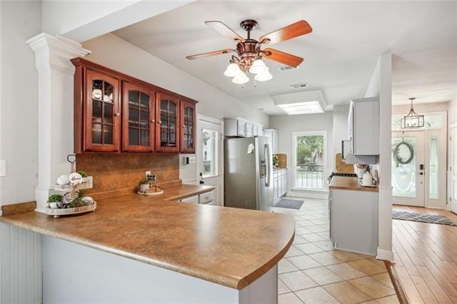 kitchen featuring ornate columns, light tile patterned floors, stainless steel refrigerator, kitchen peninsula, and ceiling fan