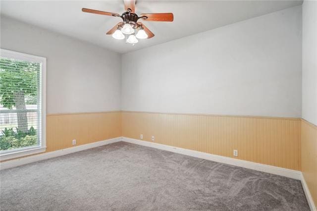 empty room with carpet floors, wooden walls, and ceiling fan