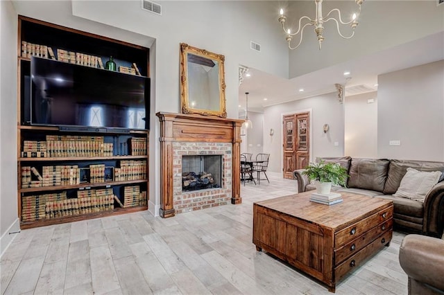 living room featuring an inviting chandelier, a towering ceiling, light hardwood / wood-style floors, and a brick fireplace