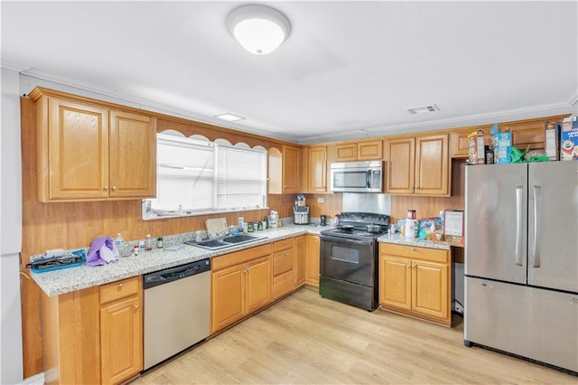 kitchen with sink, light stone counters, ornamental molding, appliances with stainless steel finishes, and light hardwood / wood-style floors