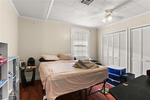 bedroom with dark wood-type flooring, ceiling fan, crown molding, and two closets