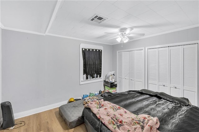 bedroom featuring crown molding, two closets, wood-type flooring, and ceiling fan