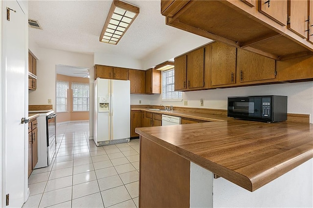 kitchen with sink, a textured ceiling, light tile patterned floors, kitchen peninsula, and white appliances