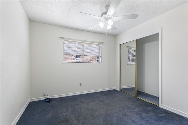 unfurnished bedroom featuring ceiling fan, dark carpet, a closet, and a textured ceiling