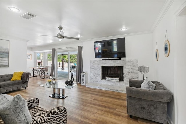 living room featuring hardwood / wood-style flooring, crown molding, a stone fireplace, and ceiling fan