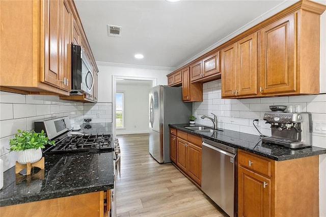 kitchen with sink, crown molding, light wood-type flooring, dark stone countertops, and stainless steel appliances