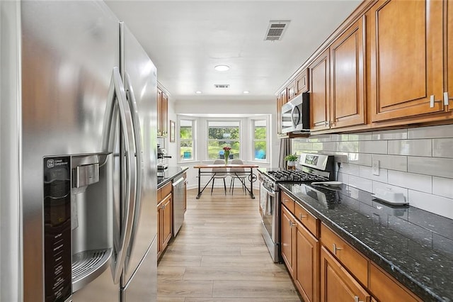 kitchen featuring dark stone countertops, tasteful backsplash, stainless steel appliances, and light hardwood / wood-style flooring