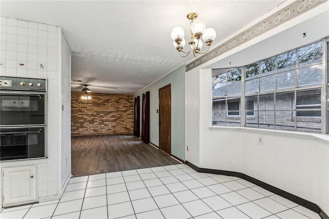 interior space featuring double oven, ceiling fan with notable chandelier, brick wall, and light tile patterned flooring