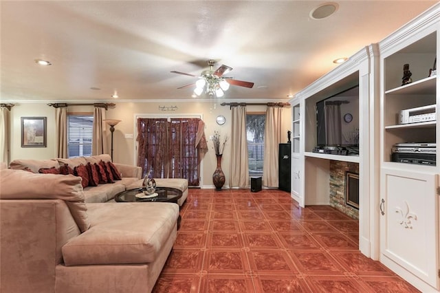 living room featuring crown molding, a stone fireplace, built in features, and ceiling fan