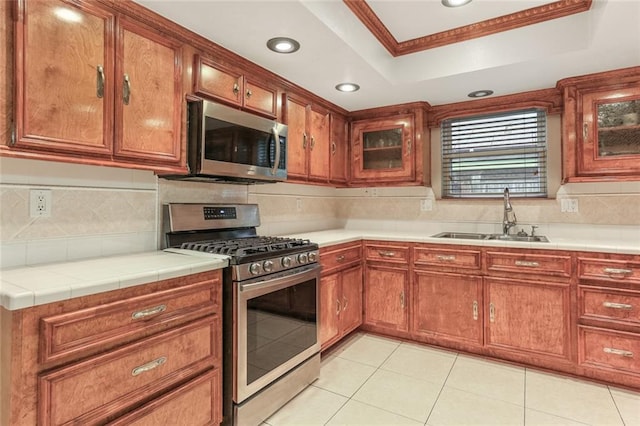 kitchen featuring sink, stainless steel appliances, tasteful backsplash, a tray ceiling, and ornamental molding