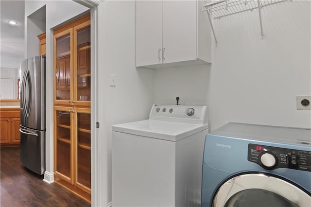 clothes washing area featuring dark wood-type flooring, cabinets, and washer and clothes dryer