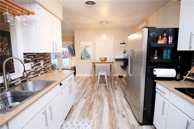 kitchen with tasteful backsplash, sink, white cabinets, hanging light fixtures, and light hardwood / wood-style flooring