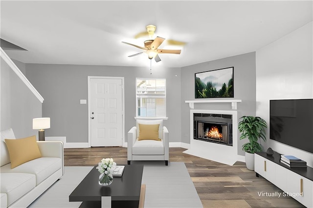 living room with a lit fireplace, baseboards, ceiling fan, and dark wood-type flooring