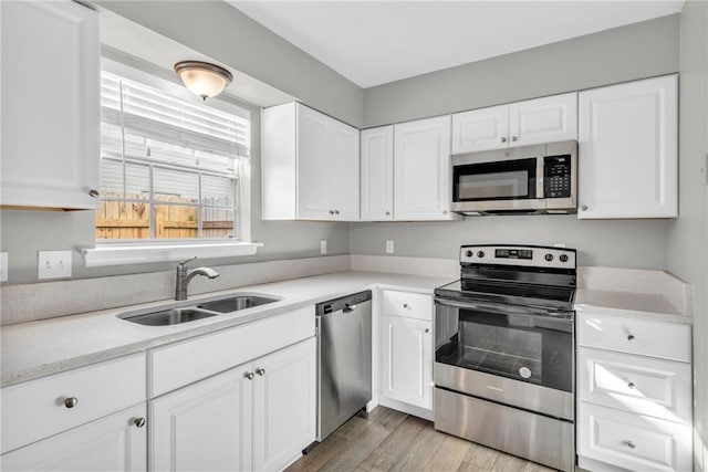 kitchen featuring light wood finished floors, appliances with stainless steel finishes, white cabinets, and a sink