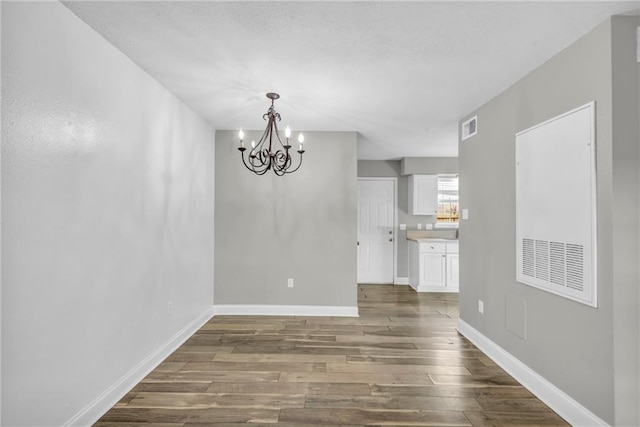 unfurnished dining area with visible vents, dark wood finished floors, baseboards, and an inviting chandelier