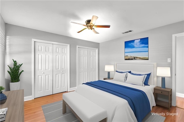 bedroom featuring wood finished floors, two closets, visible vents, and baseboards