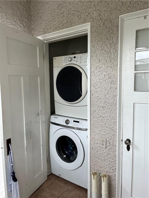 laundry area featuring dark tile patterned flooring and stacked washer and clothes dryer