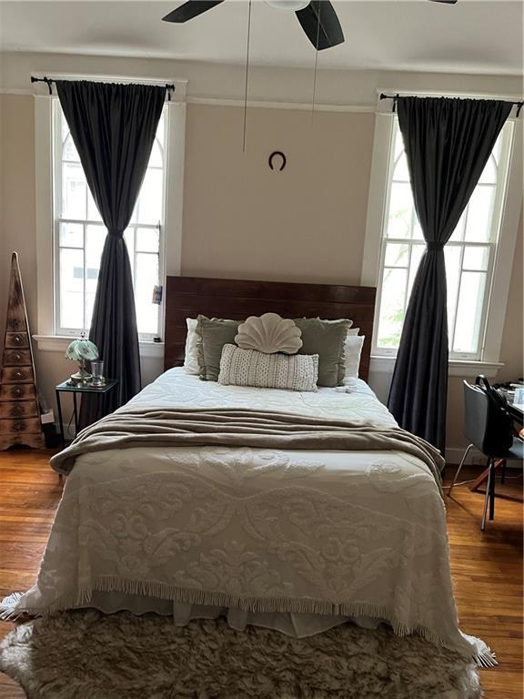 bedroom featuring ceiling fan, hardwood / wood-style floors, and multiple windows