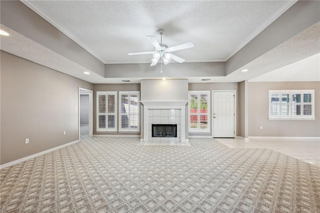 unfurnished living room with a tile fireplace, ceiling fan, a textured ceiling, and a tray ceiling